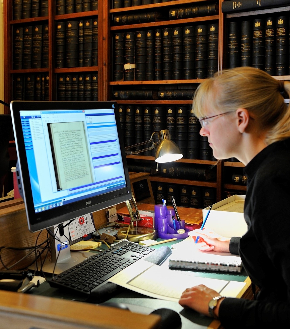 Woman sitting at computer reviewing manuscripts on a computer screen